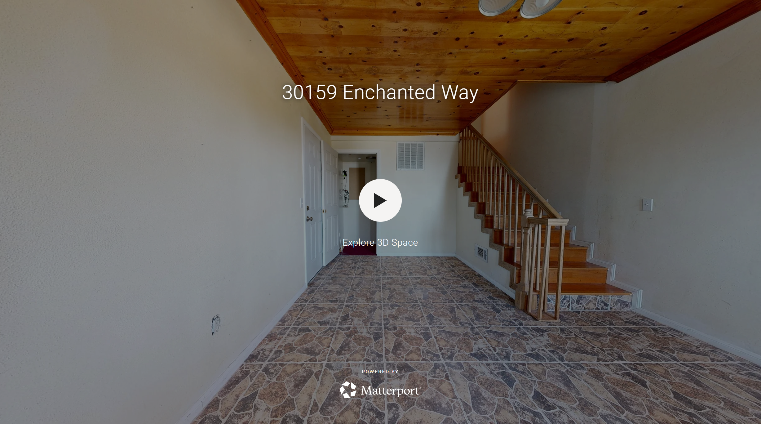 Interior view of a house entryway with tiled floor, off-white walls, a staircase with wooden steps and railing, a ceiling with wooden paneling, a white door, and some wall vents.