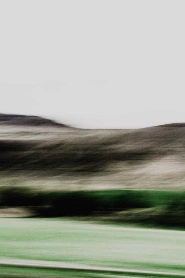 Blurred landscape with hills and grassy fields under a cloudy sky.
