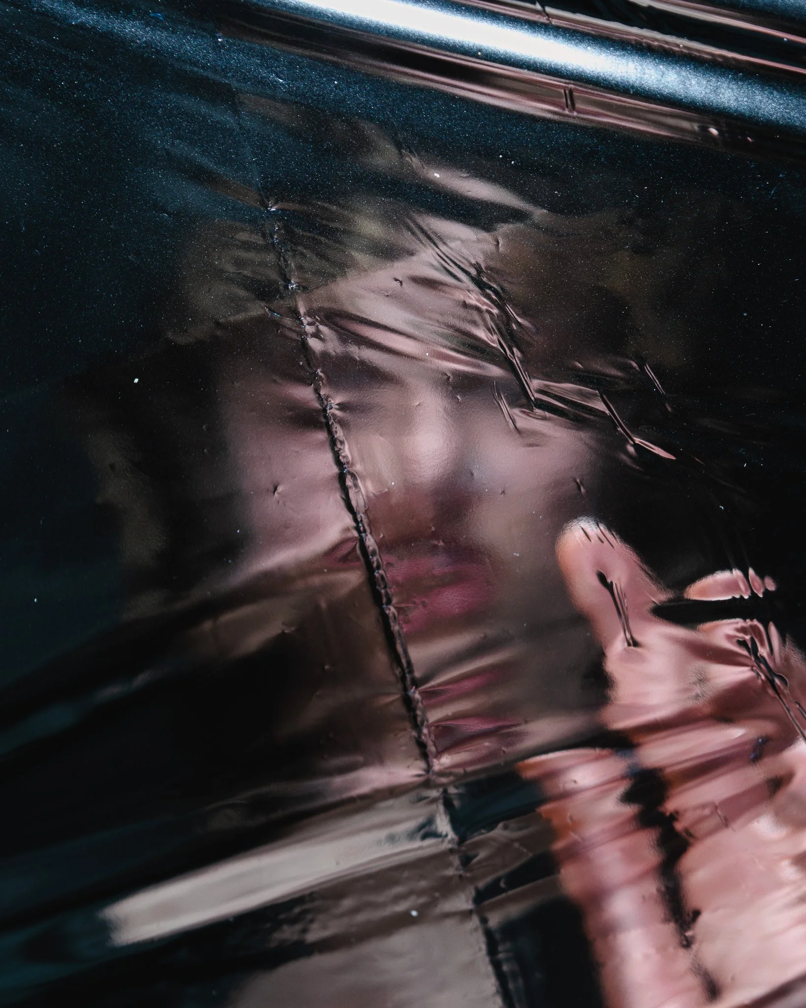 Close-up of a shiny, metallic, pinkish surface with crinkled texture and reflections.