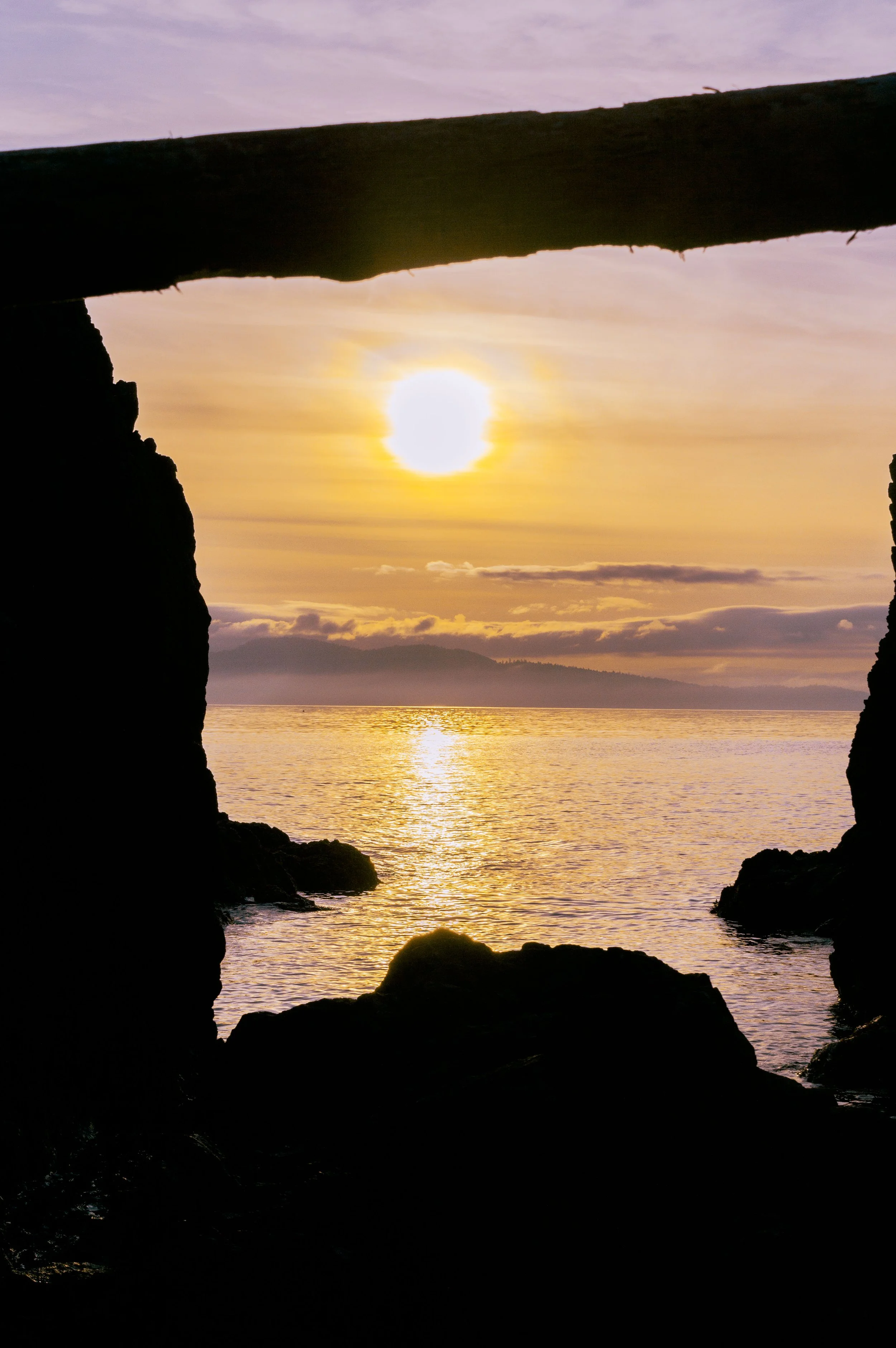 Sunset over water, viewed through a natural rock formation on the coastline.