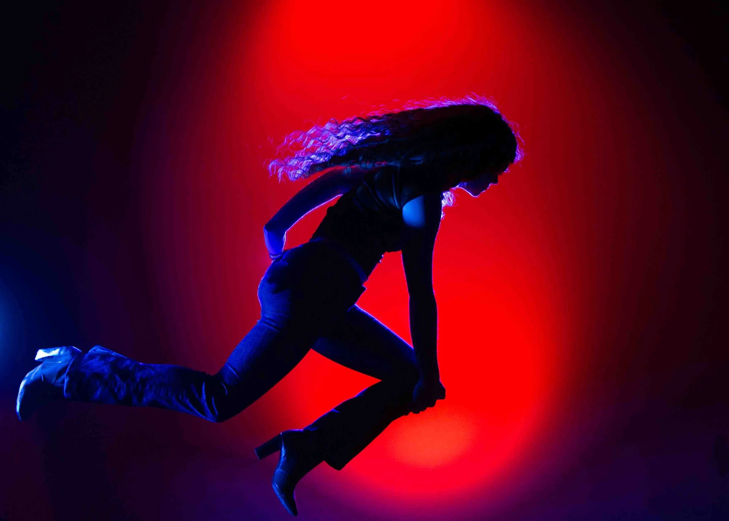 A silhouette of a person on their hands and knees with another person on their back, set against a red and black background, appearing to be performing a dance or acrobatic pose.