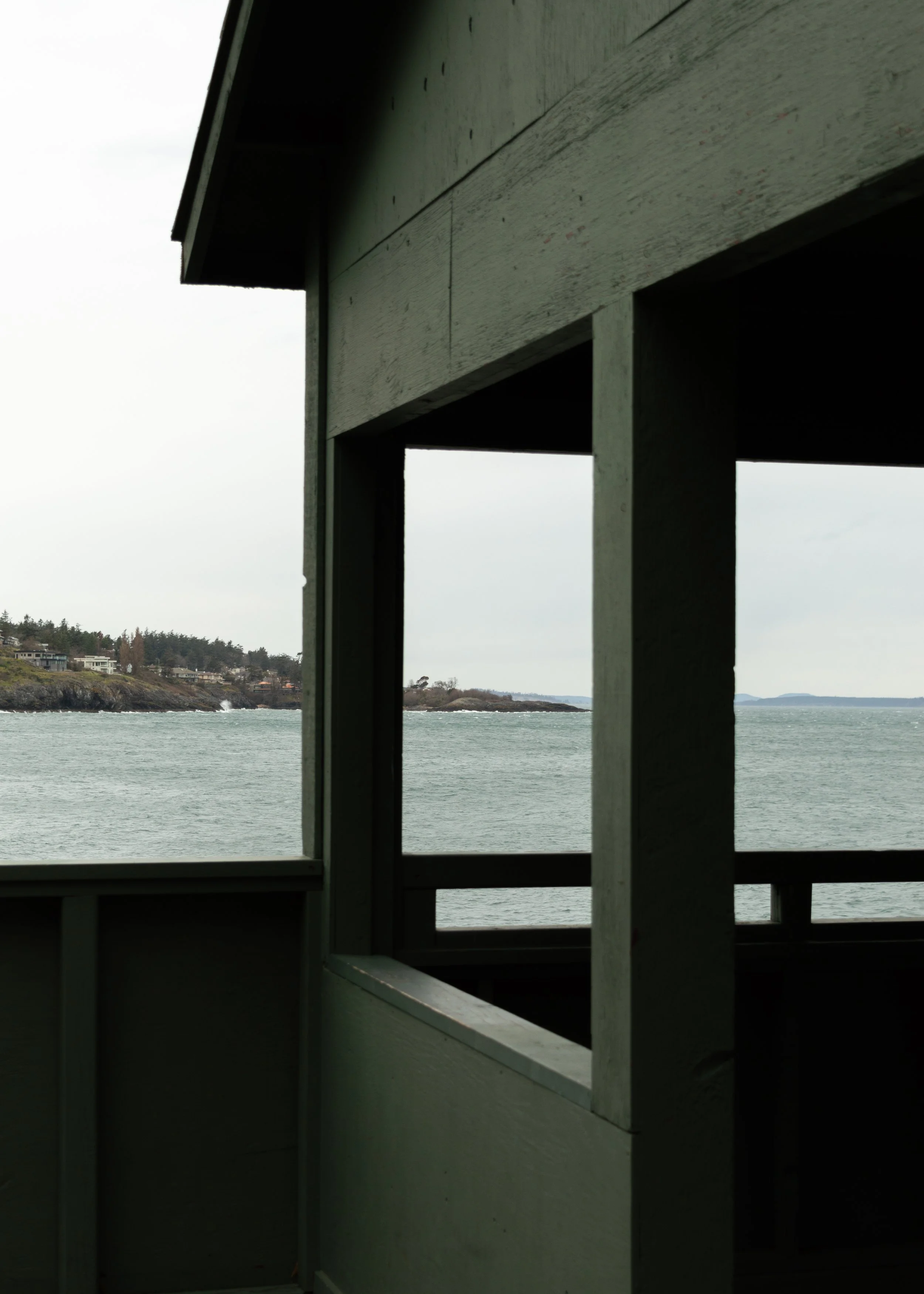 View from a house or deck overlooking a body of water with houses along the shoreline in the background, framed by a wooden structure in the foreground.