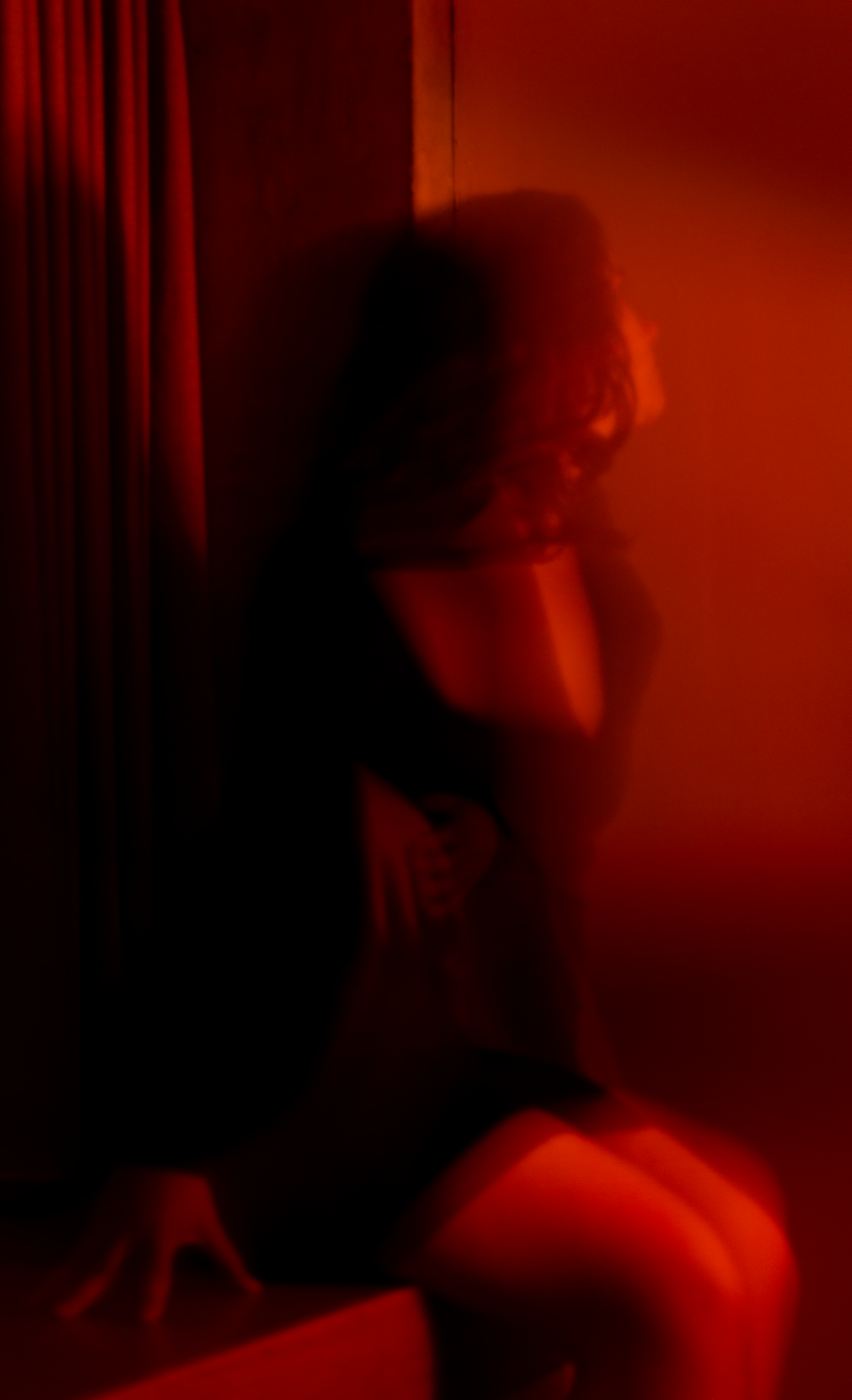 A woman with curly hair sitting on the floor, illuminated by red lighting, with her hand resting on her head.
