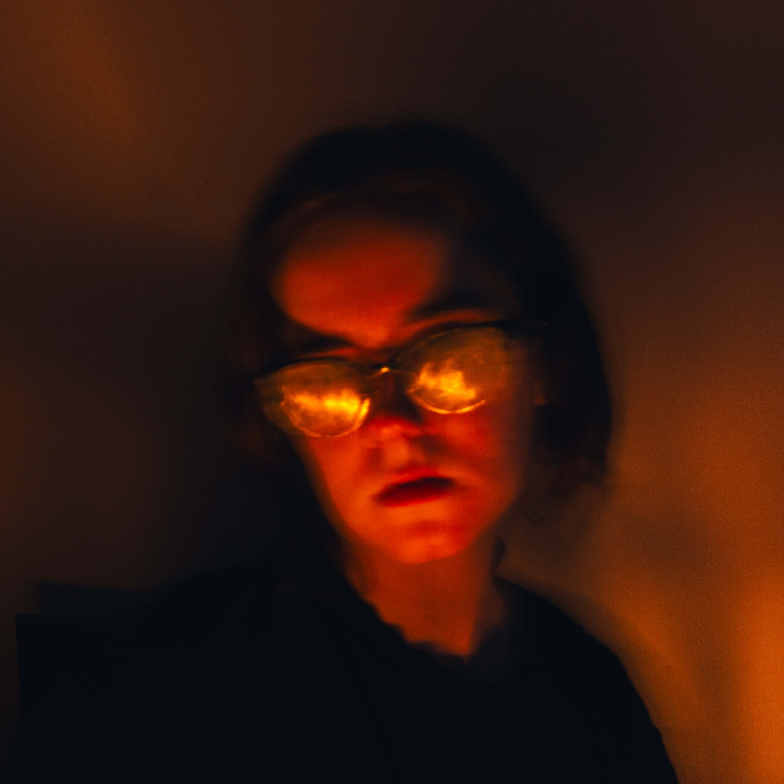 A close-up view of a person's face with reflections of orange and red lights, possibly from a fire or illuminated source, creating a warm glow on the skin.