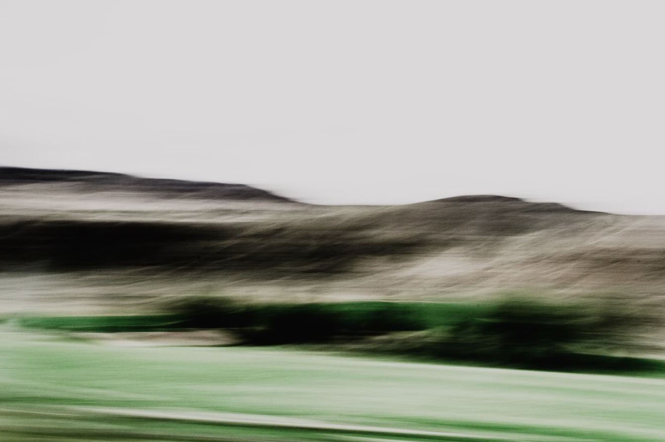 Blurred landscape with rolling hills and a grassy foreground under an overcast sky.