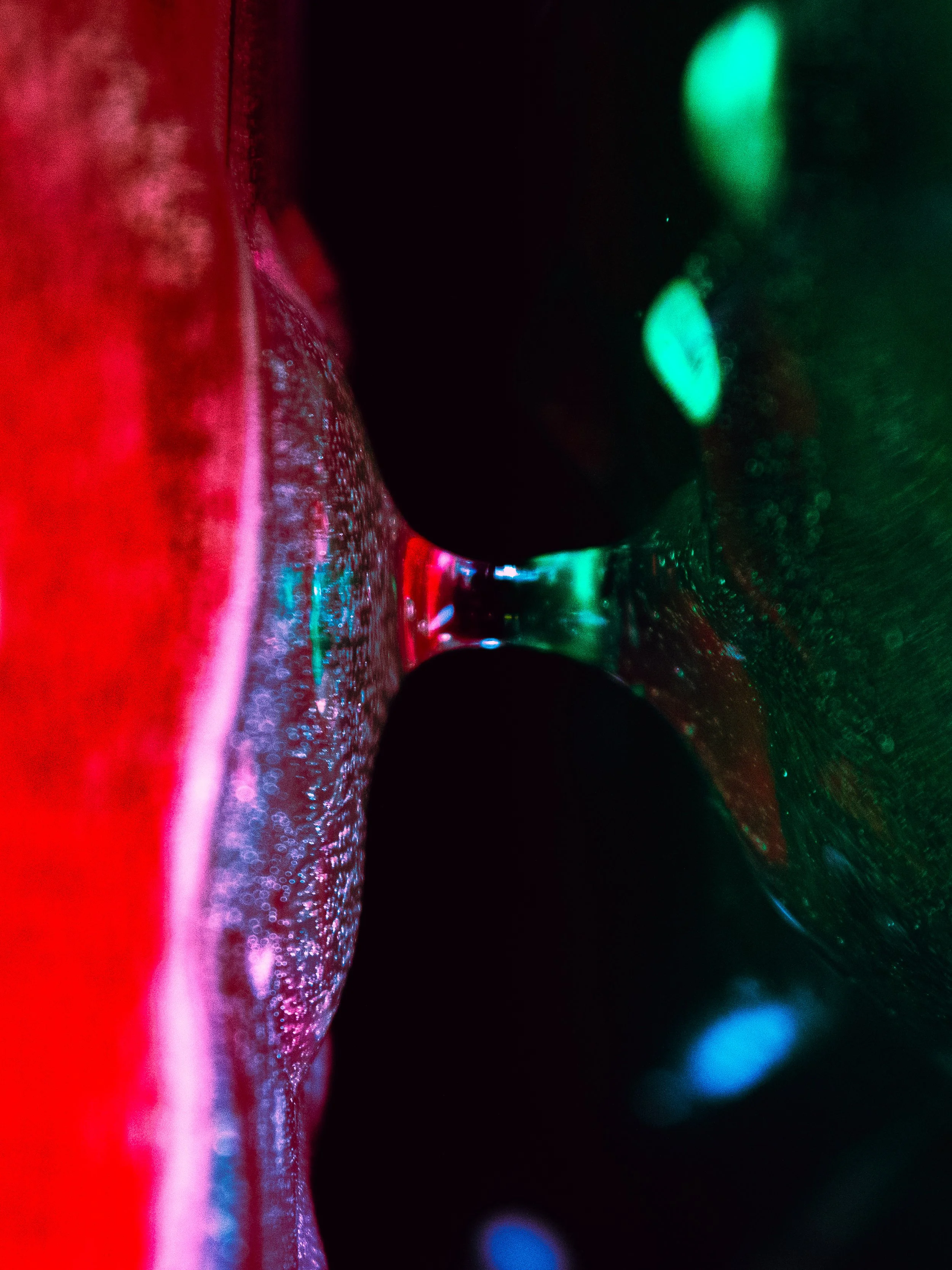 Close-up of a glass with bubbly liquid illuminated by colorful lights, creating a vibrant and abstract scene.