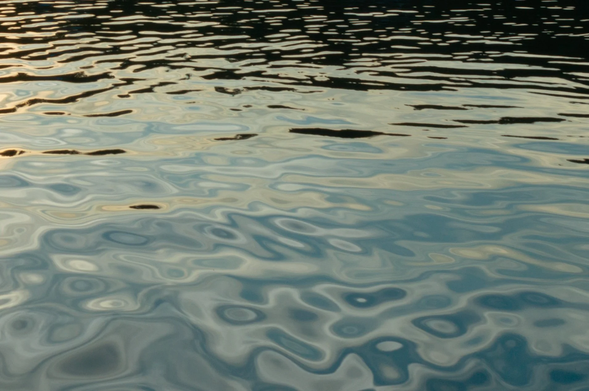 Calm water with gentle ripples, reflecting a light sky during sunset or sunrise.