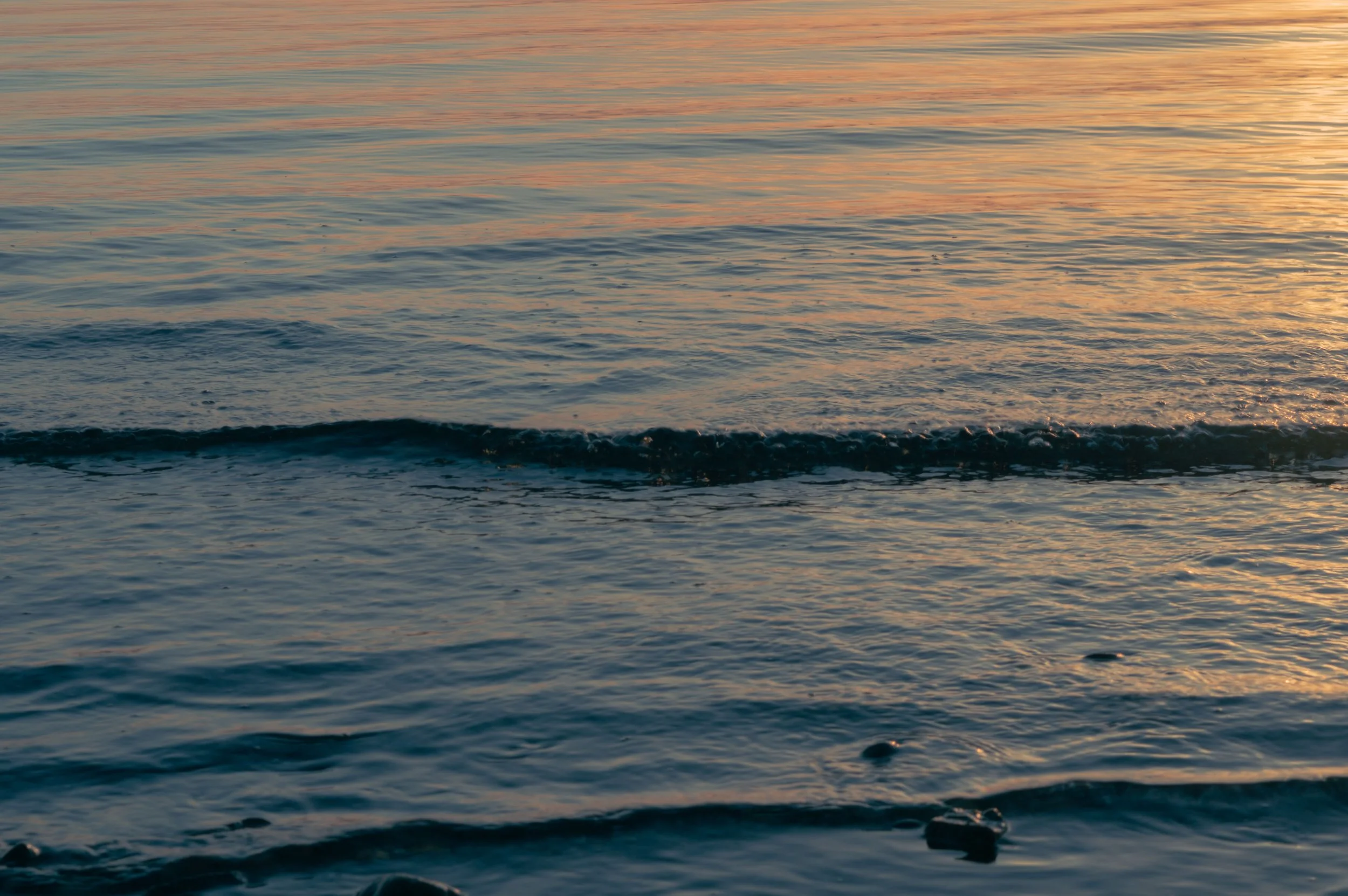 Calm ocean water with gentle waves and a colorful sunset reflection on the surface.