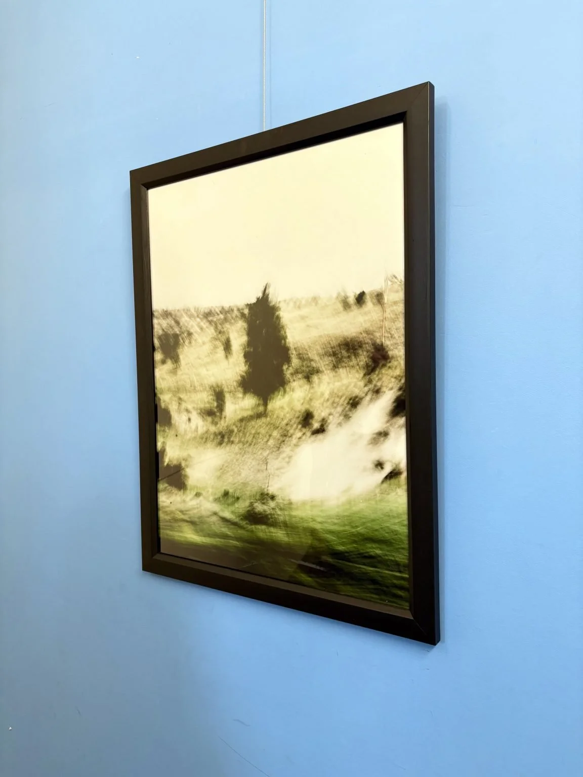Blurred landscape painting of trees and hills framed on a blue wall.