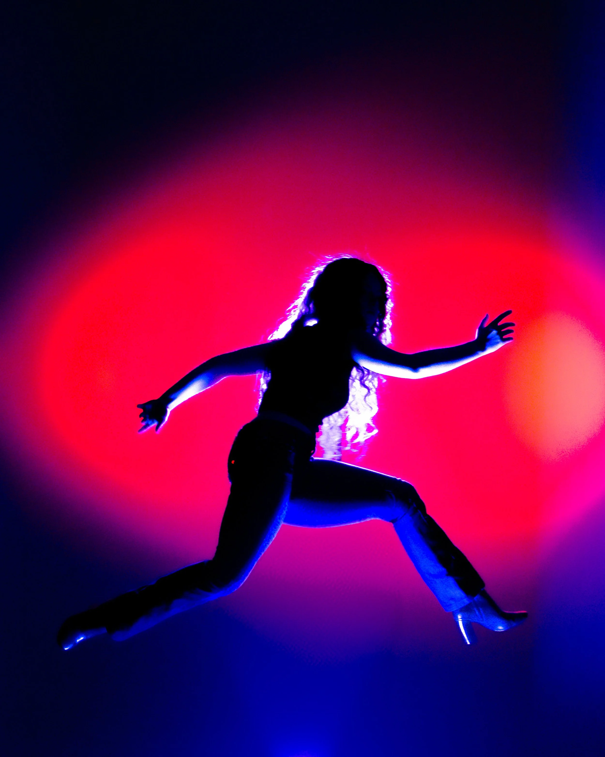 Silhouette of a woman dancing, illuminated by vibrant pink, purple, and blue neon lights, creating an abstract and energetic atmosphere.