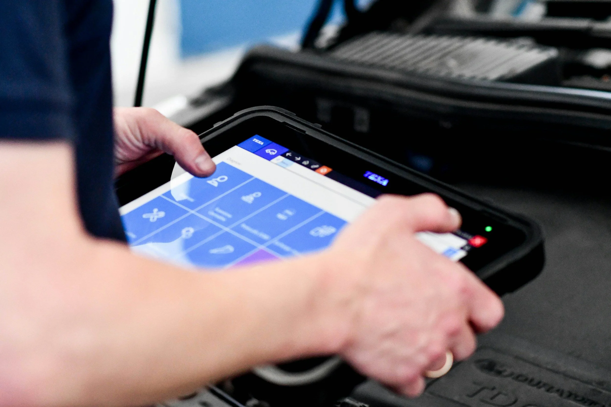 Close-up of a person's hand holding a mobile device displaying a calendar app with dates and appointment icons, with a luggage or suitcase in the background.