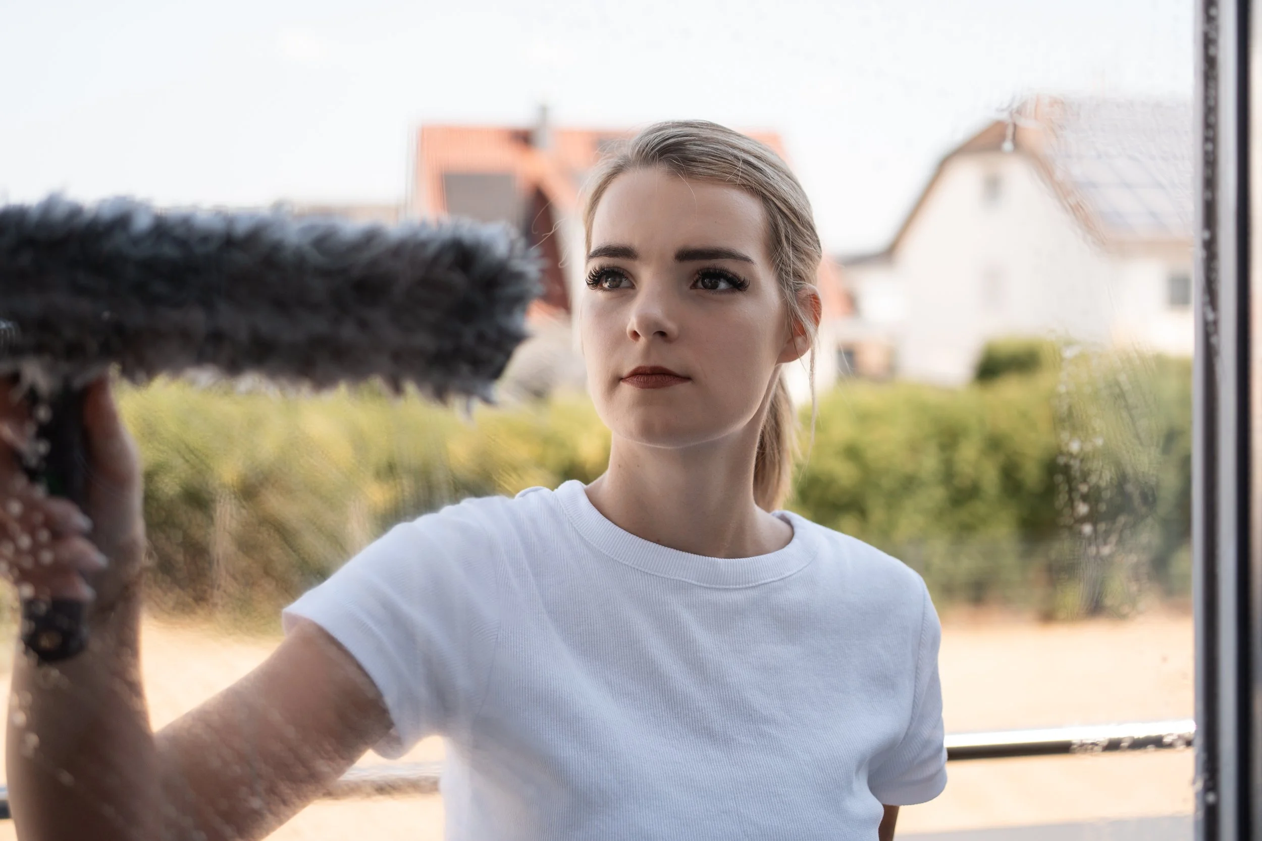 Jugendliche Frau mit braunen Haaren vor einem Fenster, während jemand korrespondiert, im Freien mit Häusern im Hintergrund.