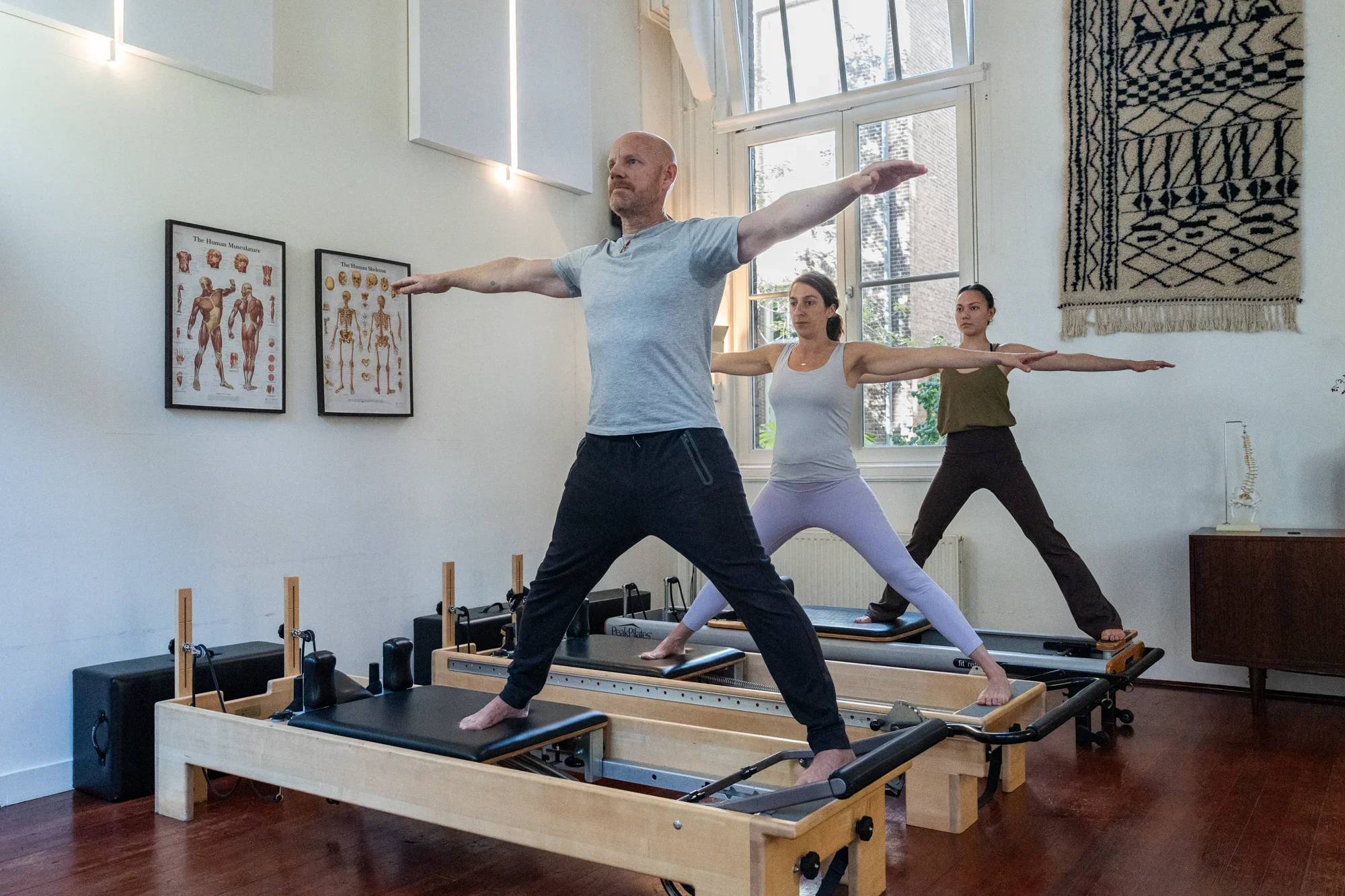 Small group Reformer Pilates class in Amsterdam West, with three people standing in a wide stance on the Reformers