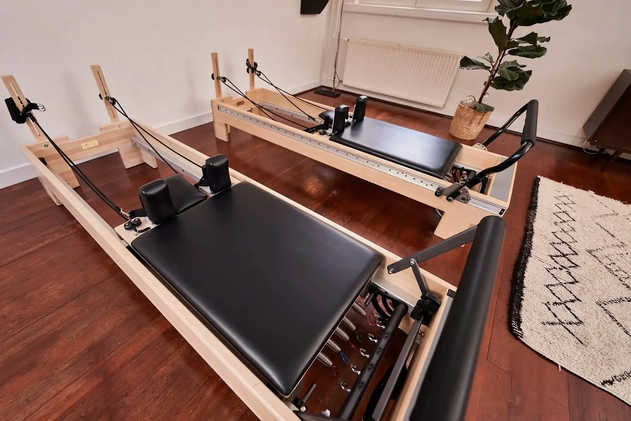 Pilates Reformers lined up on the wooden floor of the studio in Amsterdam West