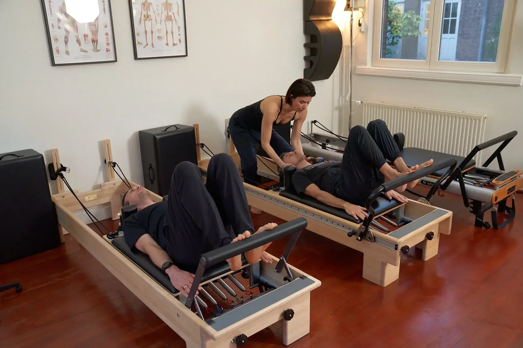 Pilates teacher guiding two clients on Reformers in a small group Trio Pilates class in Amsterdam West
