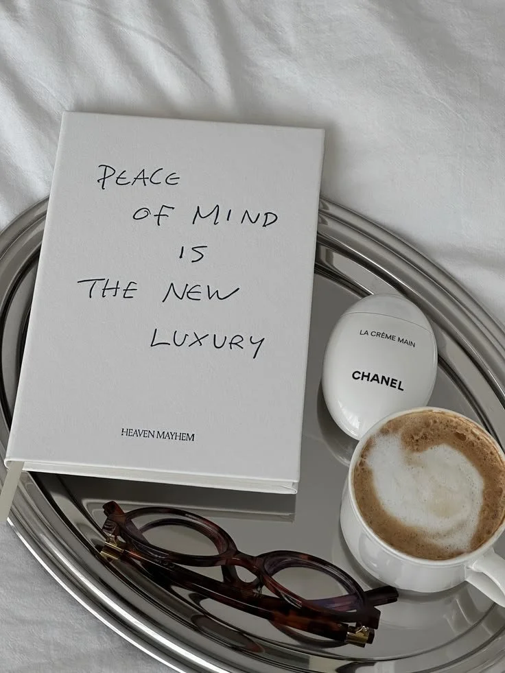 A luxury silver tray holding a pair of glasses, a cup of coffee with frothy milk, a box of Chanel hand cream, and a card that reads, 'PEACE OF MIND IS THE NEW LUXURY HEAVEN MAYHEM'.