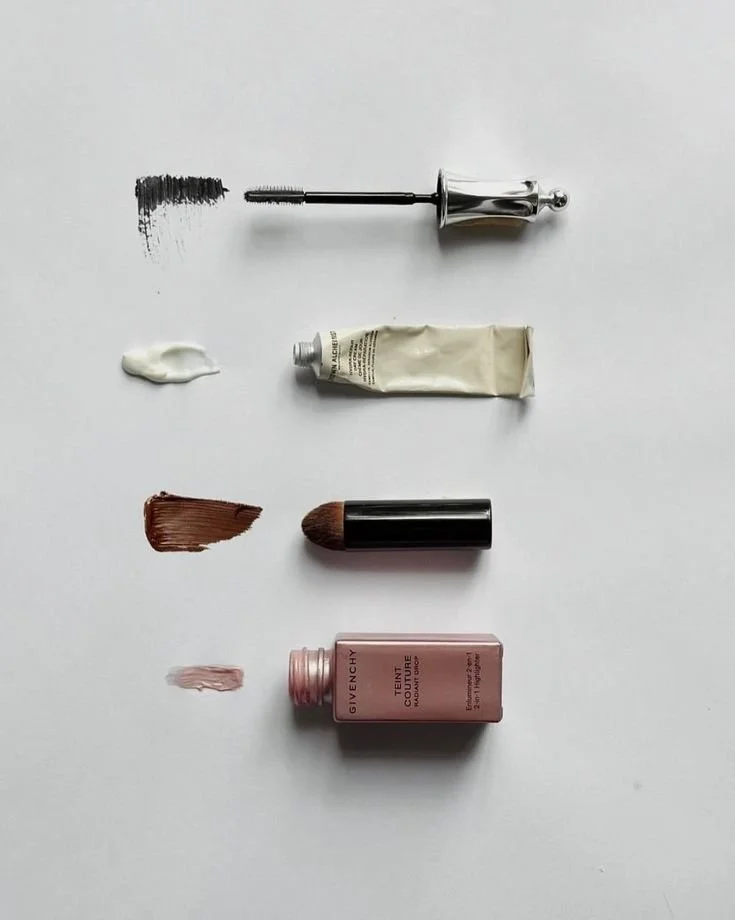 Array of makeup products with swatches on a white background, including mascara, foundation, lipstick, concealer, and lip gloss.