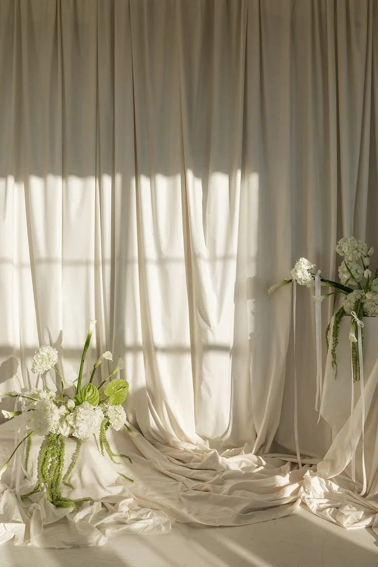 White curtains with floral arrangements on each side featuring white flowers and green leaves.