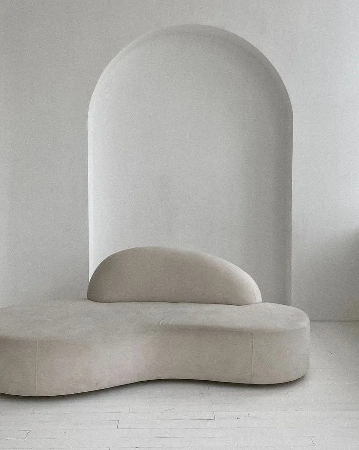 Minimalist, luxury beige sofa with rounded design against a white wall with an arched alcove.