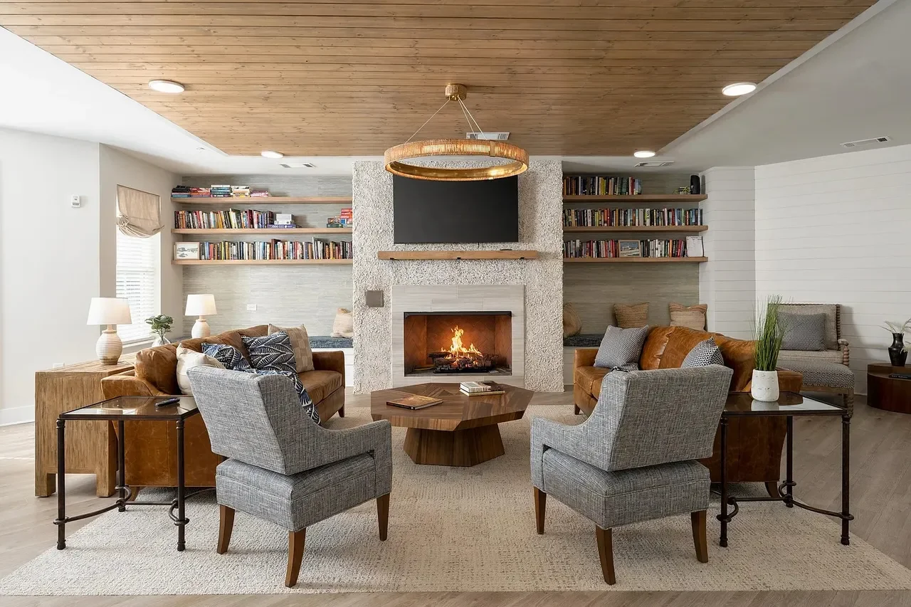 Oak Grove at Blake Farm Cozy living room with gray armchairs, brown leather sofas, a fireplace, bookshelves, and decorative lamps.