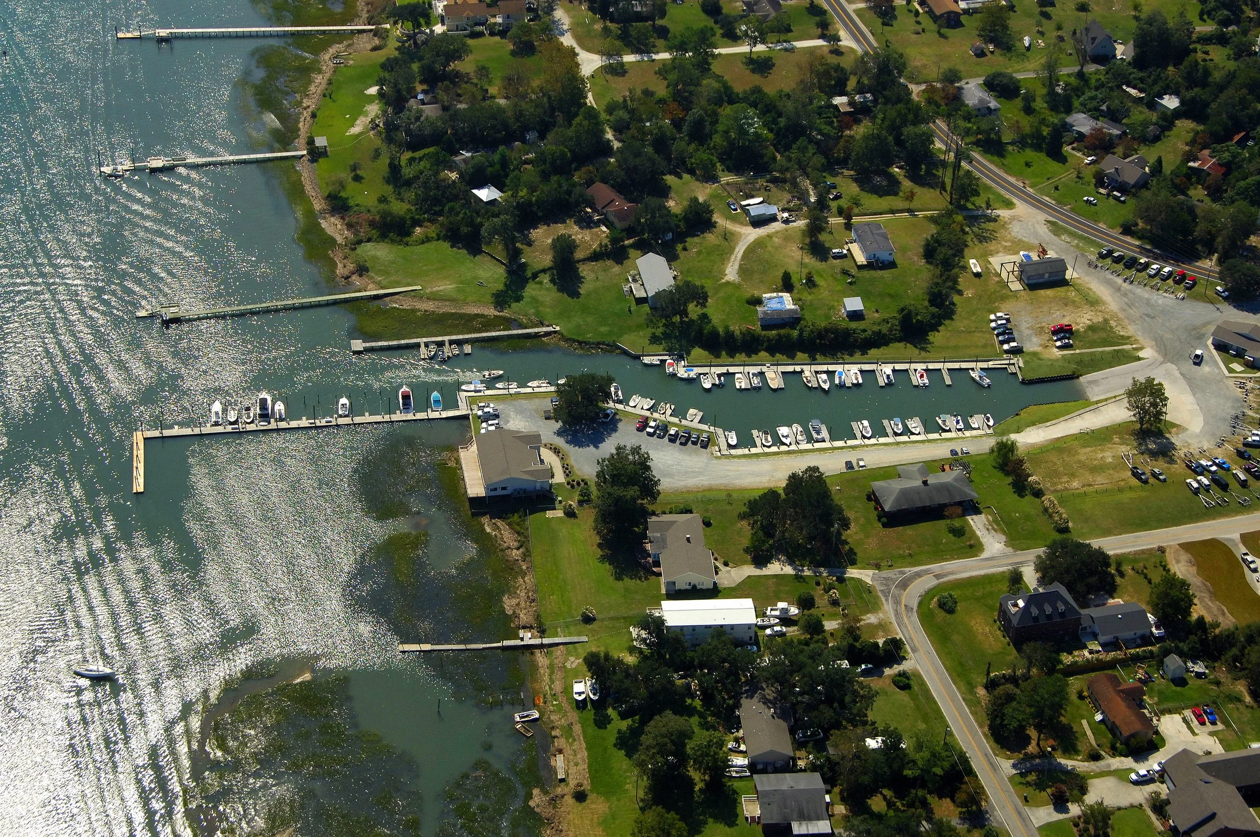 Scott's Hill NC Wilmington NC Aerial view of a residential area by a waterway with boats docked at a marina. The neighborhood has houses, trees, roads, and parking areas.