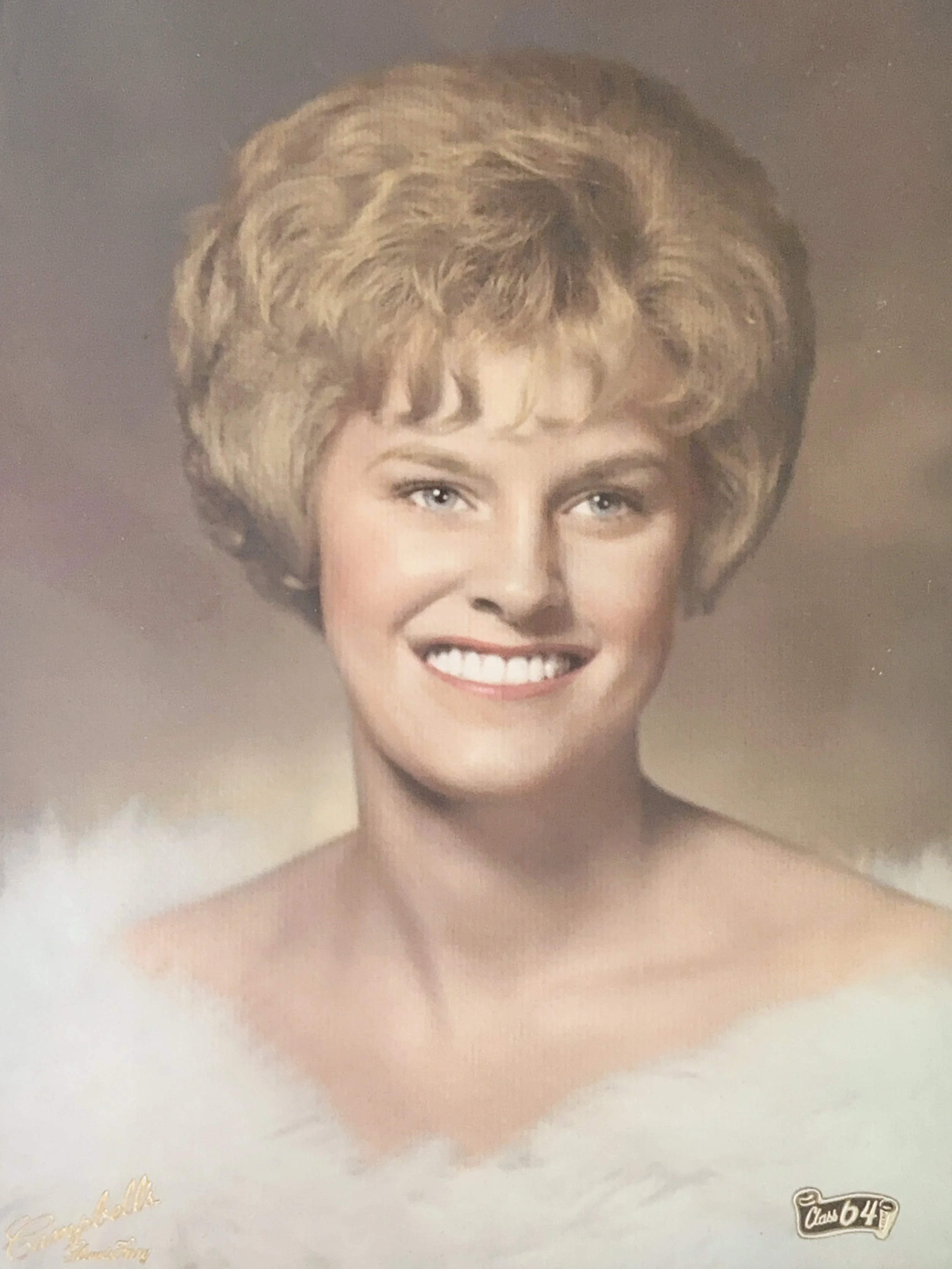 A vintage portrait of a woman with short, blonde, curly hair and a wide smile showing her teeth. The background is a neutral gradient, and there is gold cursive text in the lower left corner and a small logo with 'Class 64' in the lower right corner.