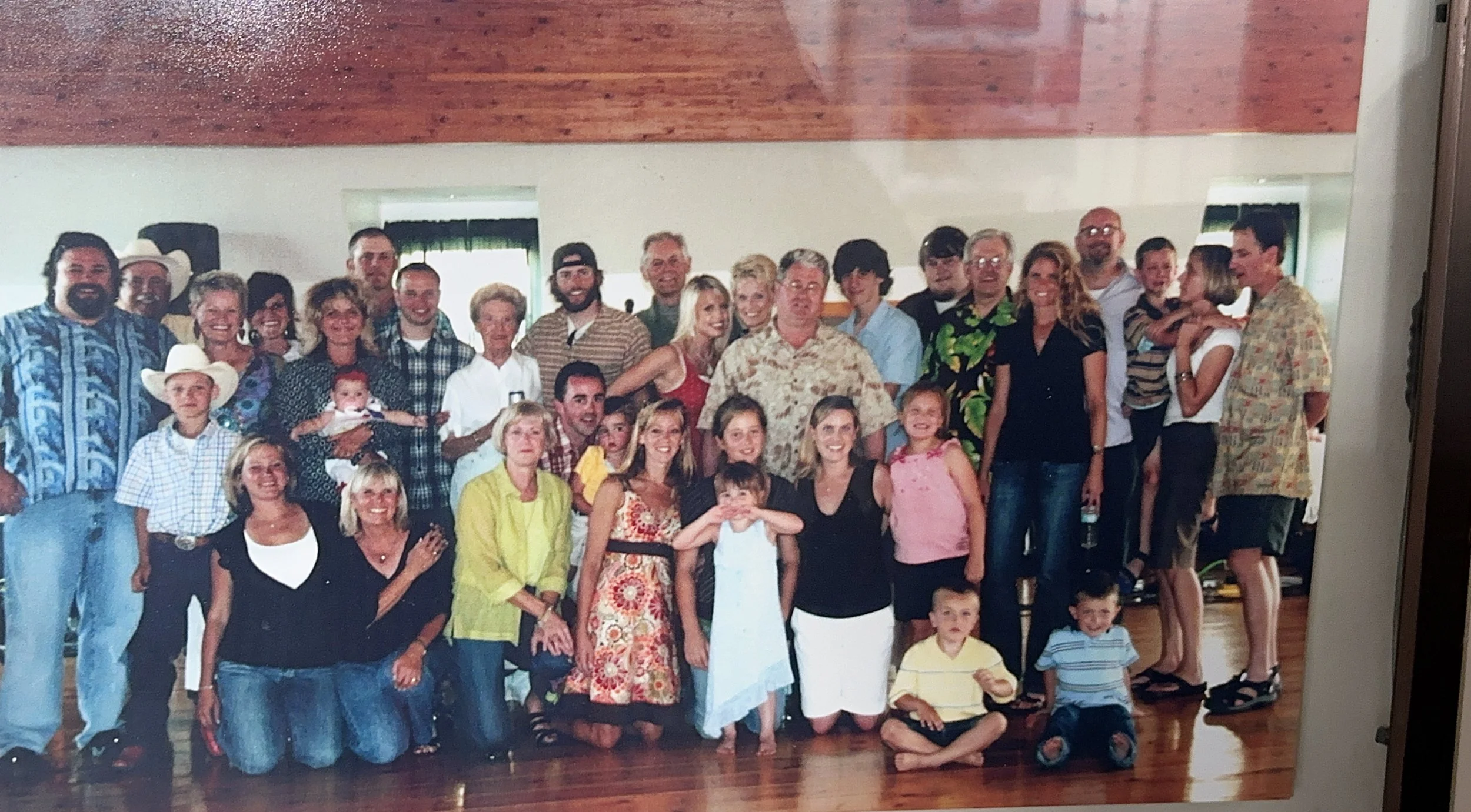 Group of people and children posing for a photo at a gathering or party in a room with wooden flooring and light-colored walls.