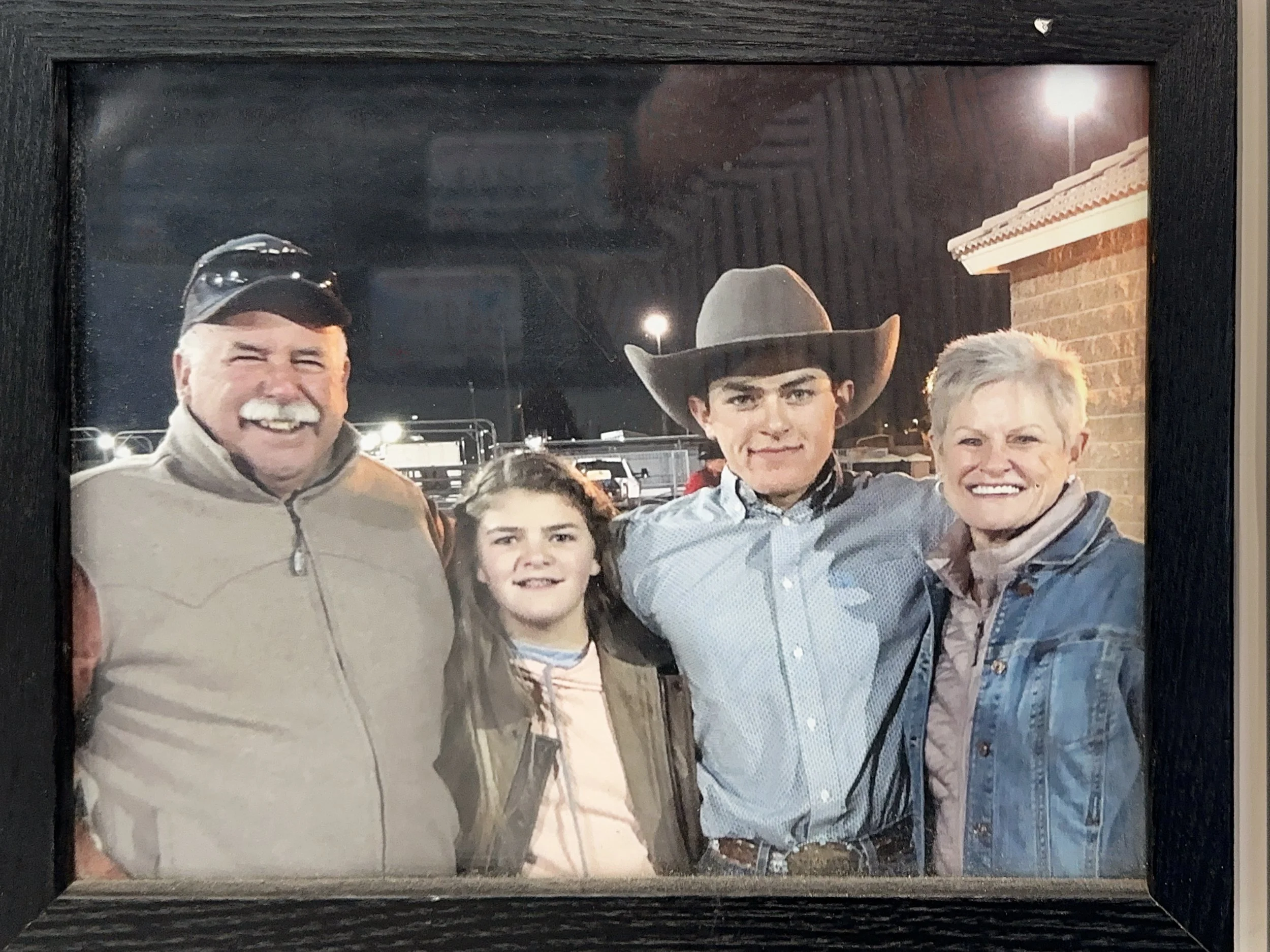 Family photo of four people, two men, a woman, and a child, smiling outdoors at night, with streetlights and a building in the background.