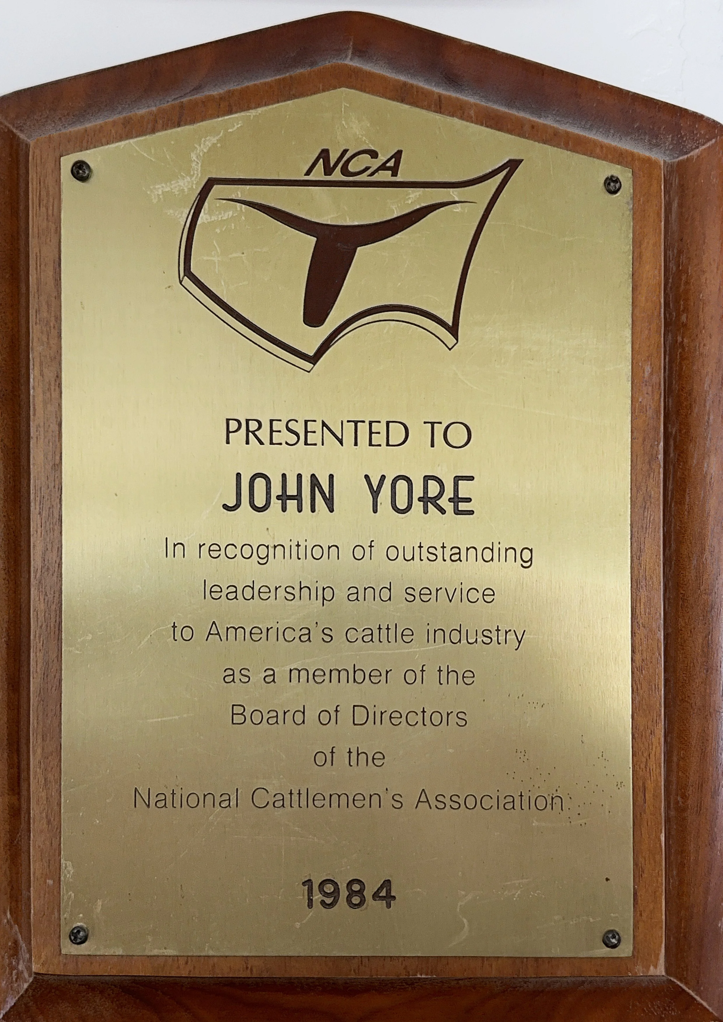 Plaque with NCA logo and text acknowledging John Yore for leadership and service to the cattle industry, dated 1984.