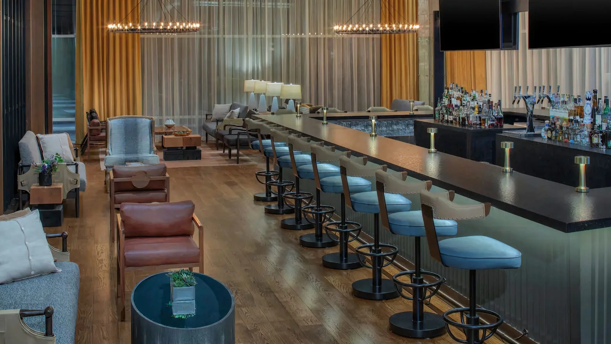 Modern bar with a long counter, bar stools, liquor bottles, and TV screens