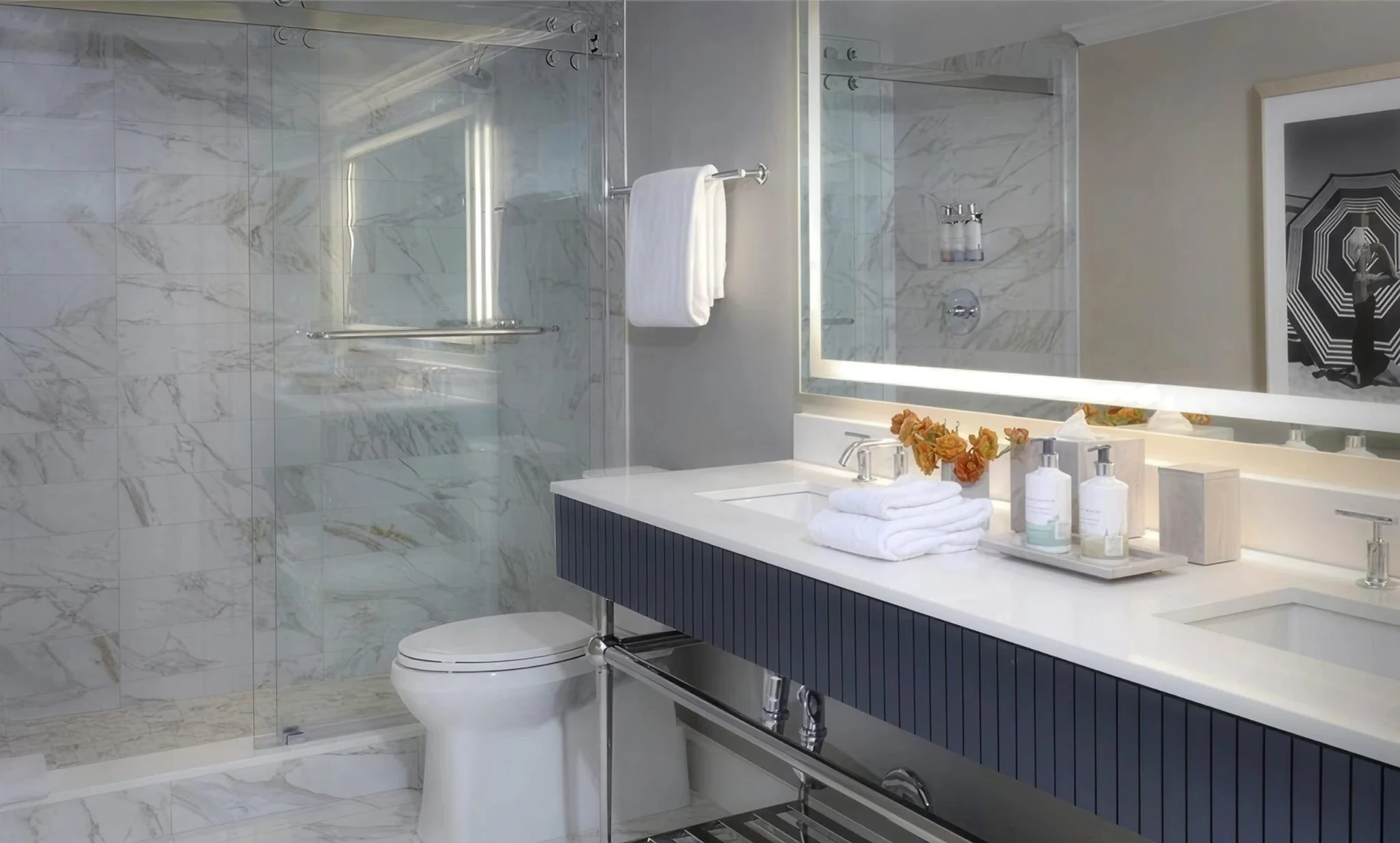 A modern bathroom featuring a marble tiled shower, a white toilet, a white countertop with a vanity mirror, and various toiletries neatly arranged. The bathroom has a sleek design with a black and white color scheme.