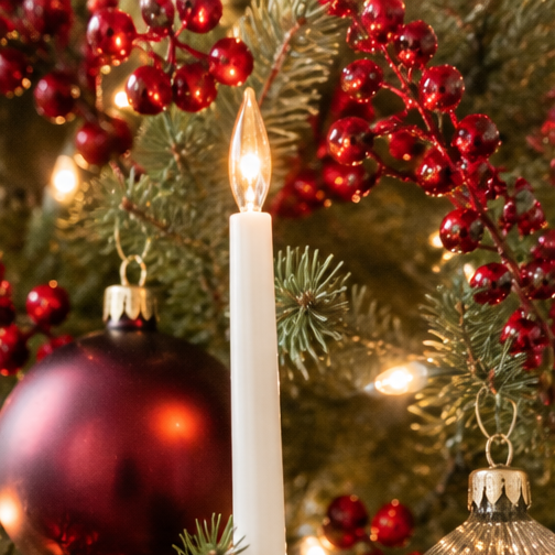 Close-up of a Christmas tree with red berries, a metallic ornament, a candle-shaped light bulb, and other decorations.