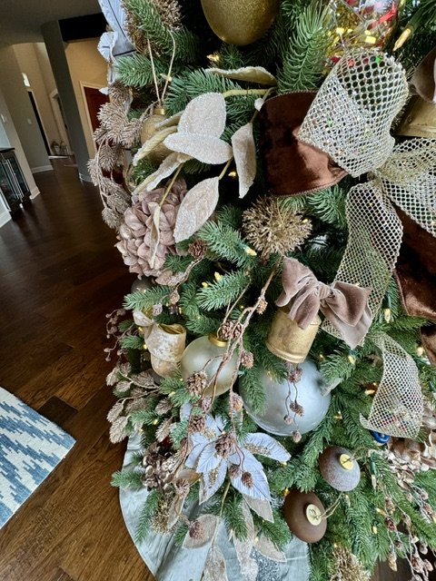 Decorated Christmas tree with gold and silver ornaments, ribbons, and pinecones inside a home.