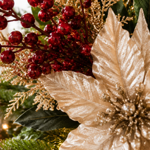 Close-up of holiday floral arrangement with red berries, gold glittered leaves, poinsettia, and greenery.