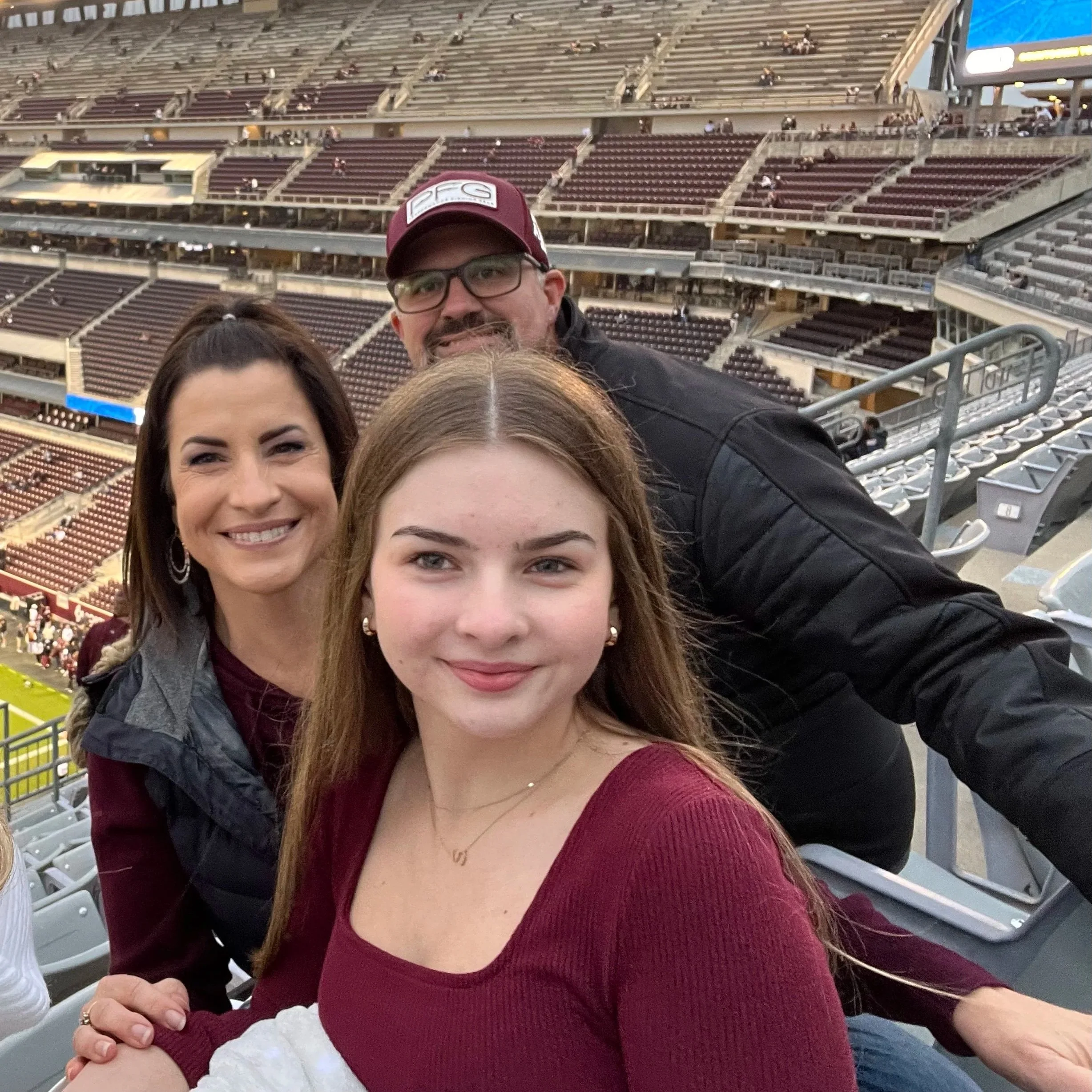 Group of people taking a selfie at a stadium, with empty seats in the background.