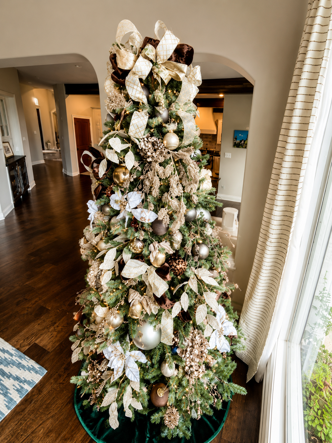 Decorated Christmas tree with gold, silver, and white ornaments, ribbons, and pinecones in a living room.