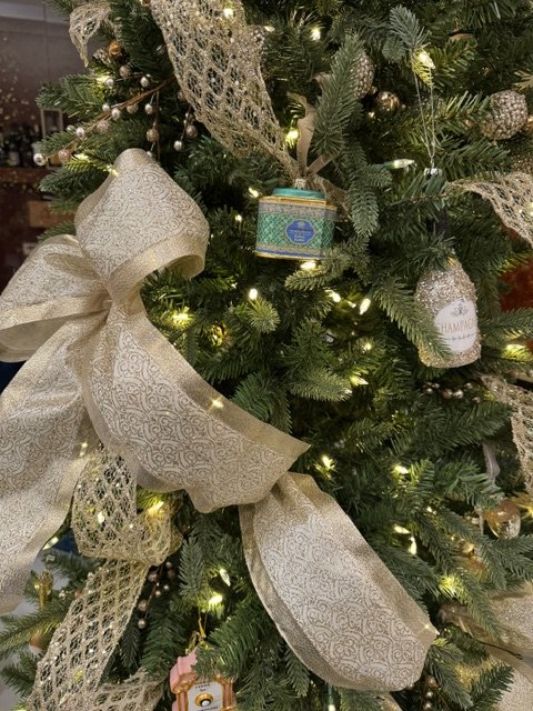 Close-up of a decorated Christmas tree with a large gold ribbon bow, lights, and ornaments.