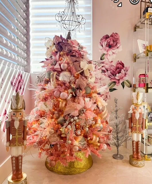 Decorated pink Christmas tree with ornaments in a pink-themed room decorated with large pink and purple flower wall art, nutcracker figures, and festive decor.