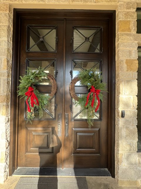 Wooden front door decorated with two Christmas wreaths with red bows.