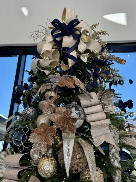 A decorated Christmas tree with ribbons, bows, ornaments, and gold and silver accents, topped with a large bow.