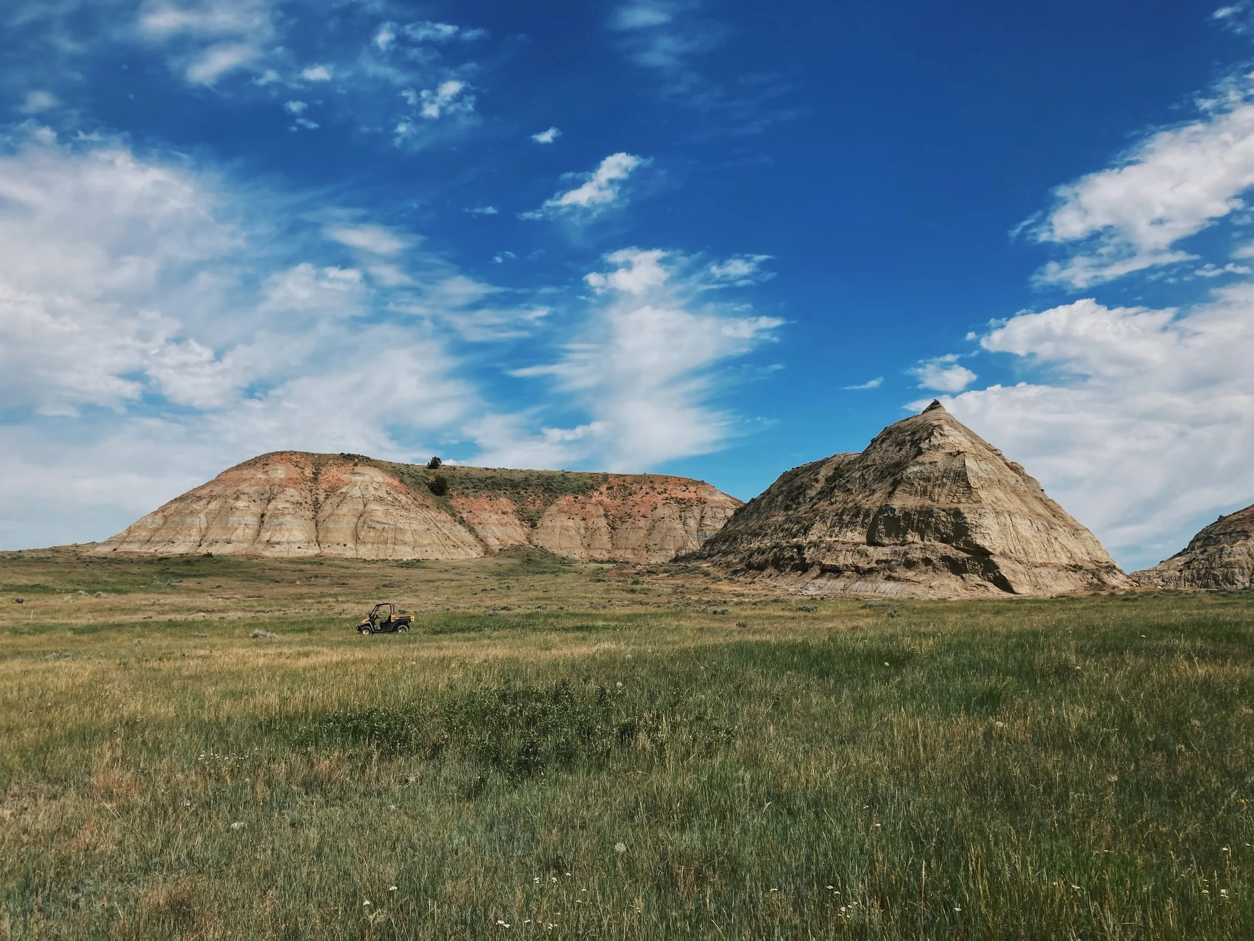 Open grassy plain with colorful layered hills in the background and a partly cloudy blue sky.