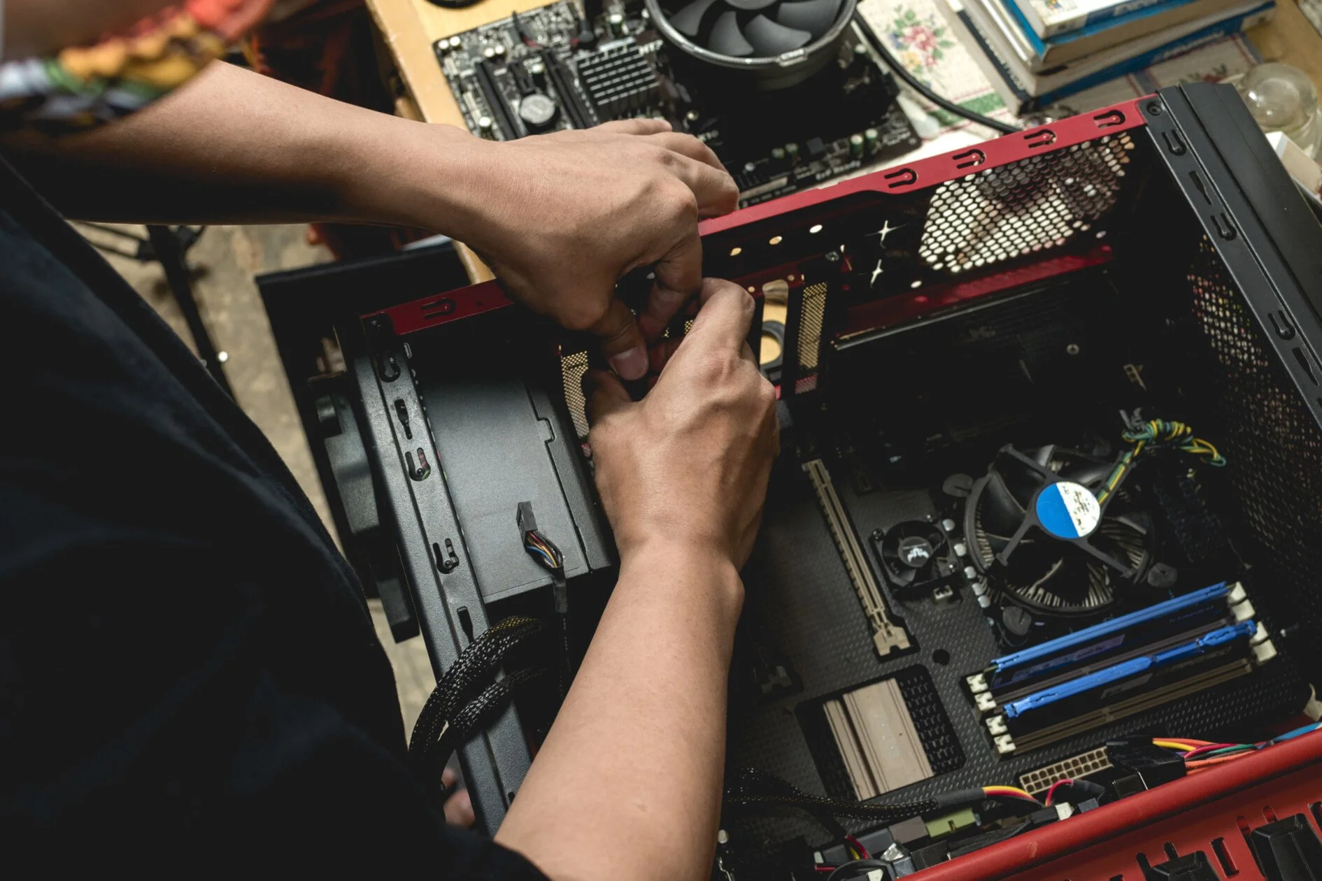 Person installing or repairing internal components of a desktop computer, with the computer case open and various parts visible