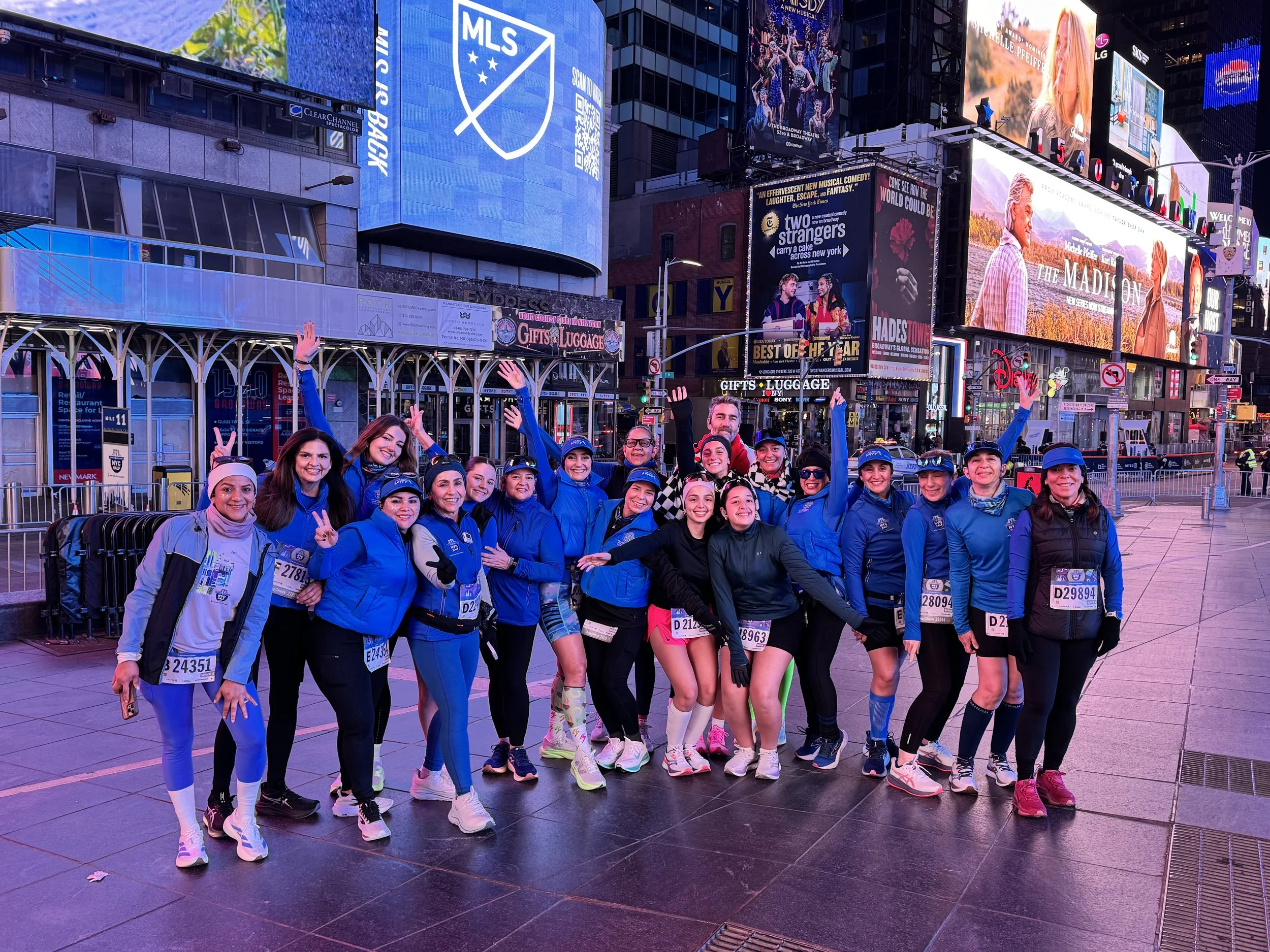 We Run Happy runners celebrating Heidy Arellano’s 100th Half Marathon at the United Airlines NYC Half Marathon in Times Square, showcasing the community and destination race experiences supported by LATAM Marathon Experience.