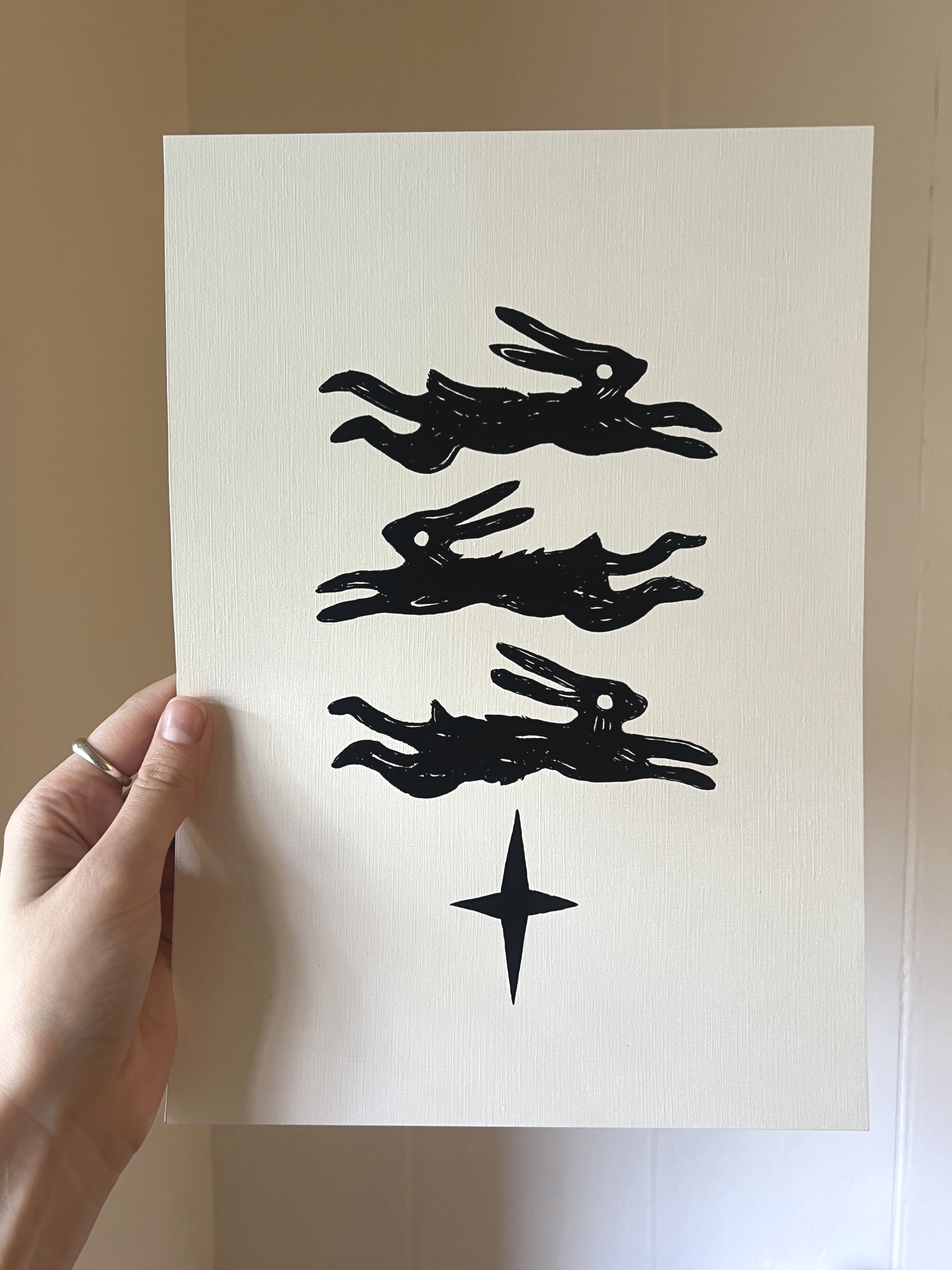 Gouache painting on paper of three black rabbits jumping, stacked on top of each other, all above a star