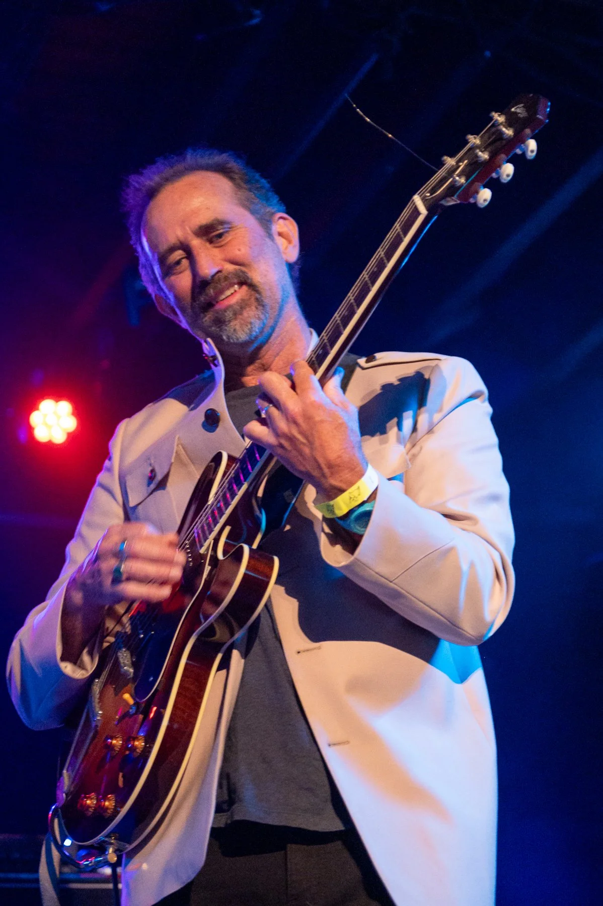 A man with a beard and mustache playing an acoustic guitar on stage under colorful stage lighting.