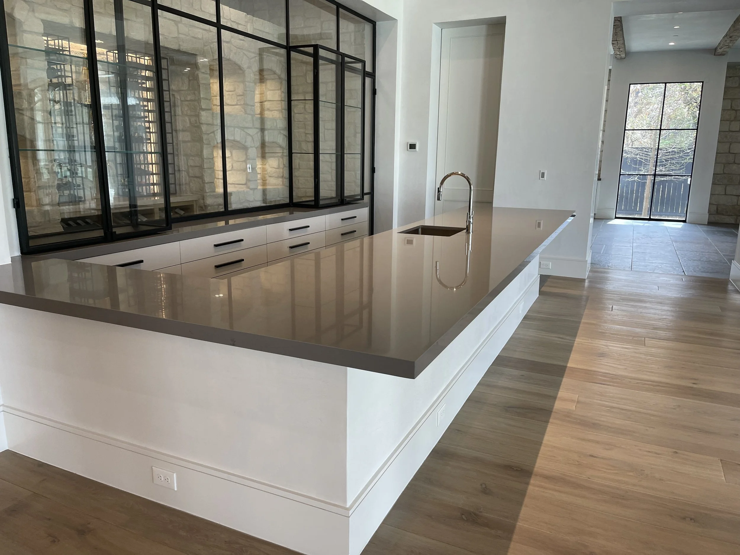 Modern kitchen island with a dark stone countertop, white waterfall base and wood cabinetry. Custom Stone Kitchen Countertops Houston, ‪713-568-5758‬
