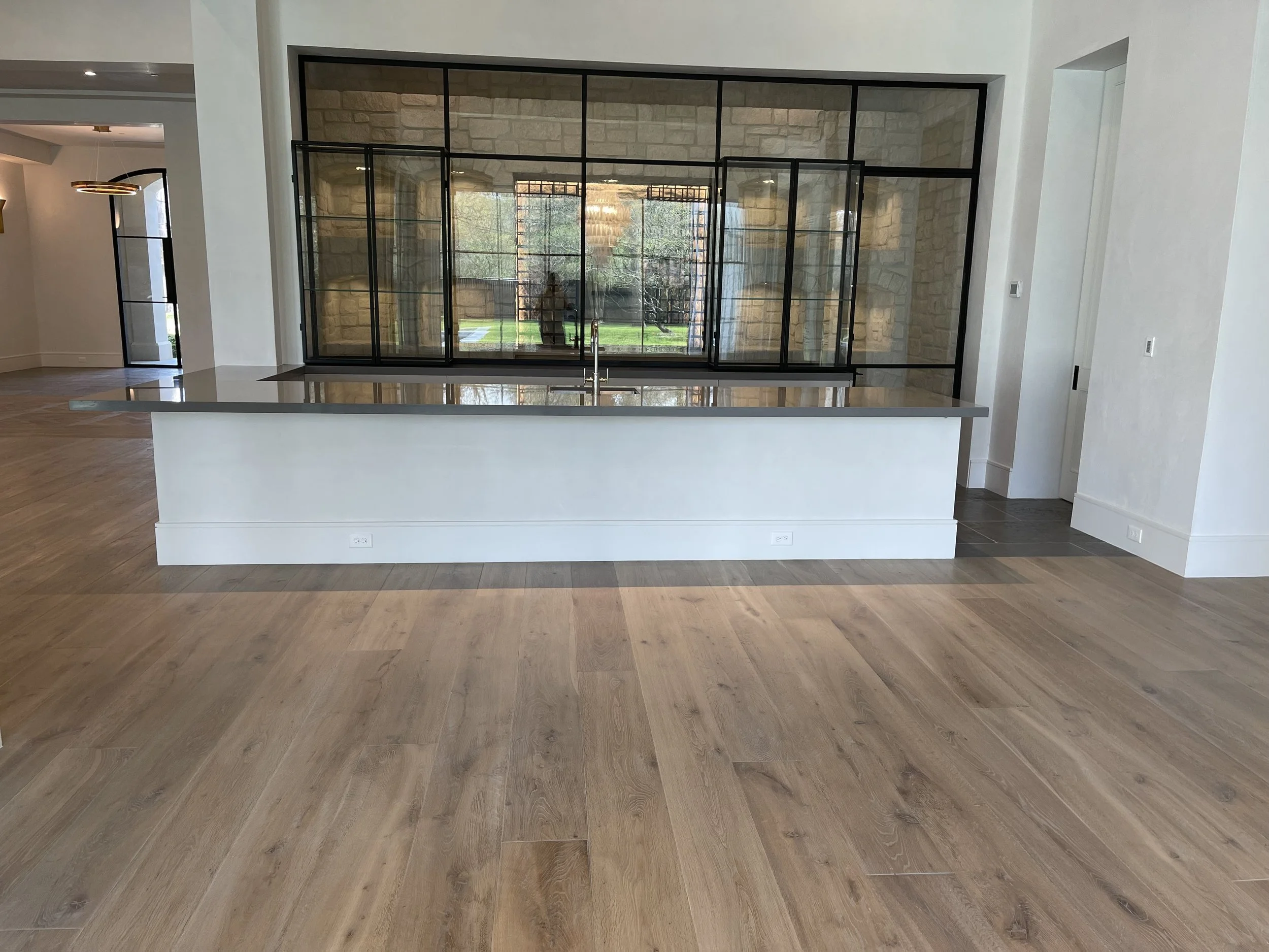 Long dark stone serving counter with black-framed glass cabinetry and natural wood flooring.
