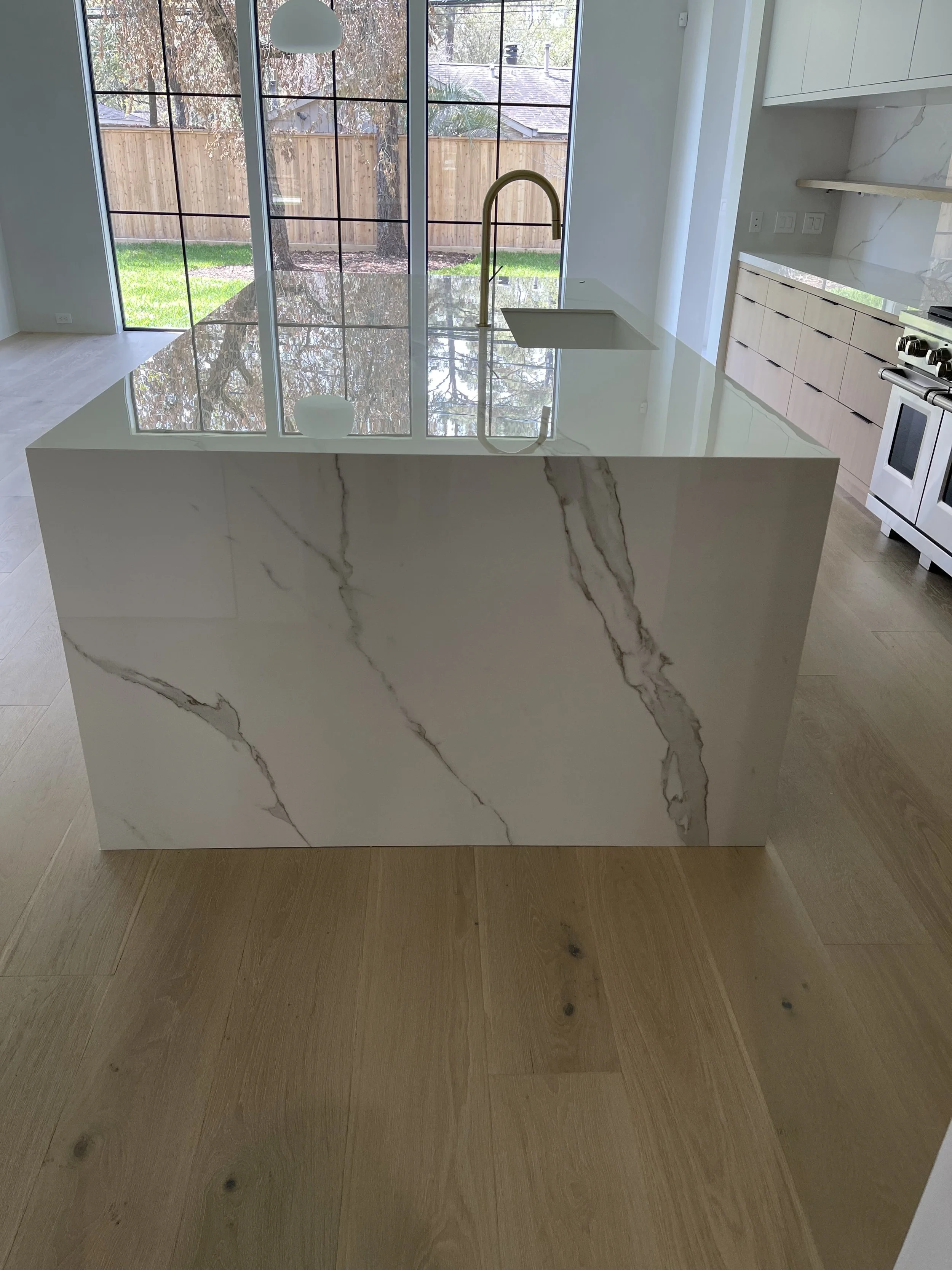 Waterfall kitchen island featuring dramatic stone veining and a polished surface. Custom fabrication, installation, Stone Kitchen Countertops Houston, ‪713-568-5758‬