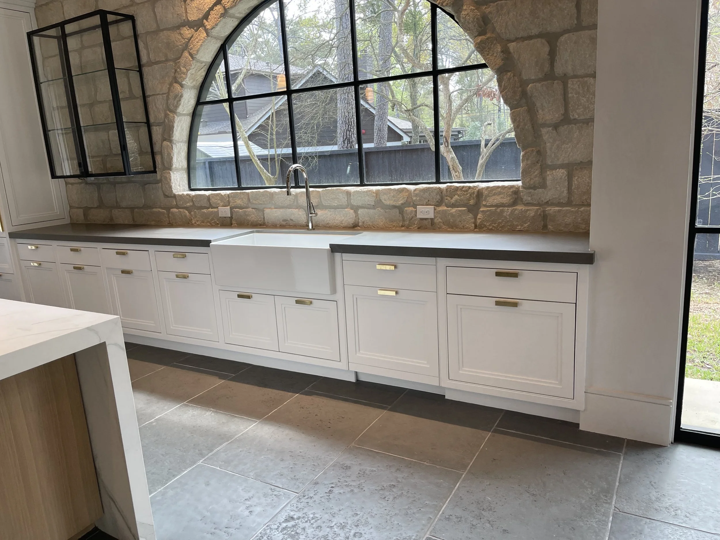 White kitchen countertops and custom cabinetry beneath a large black-framed arched window.