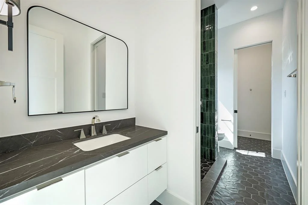 Modern white bathroom with a double vanity, dark stone countertop and black hexagon tile floor in Houston, TX.